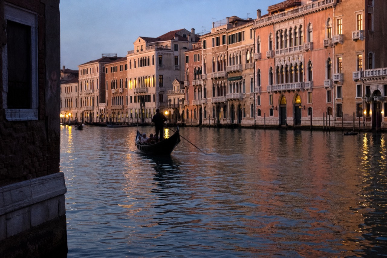 Venetian canal at golden hour with warm light on the palace fronts and a gondola silhouetted against the reflection