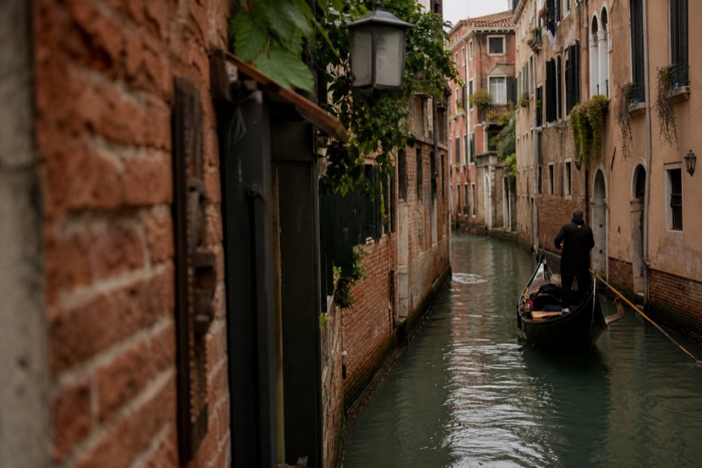 A private gondola drifting past shuttered windows and a hanging lantern in a narrow back canal, no other boats in sight