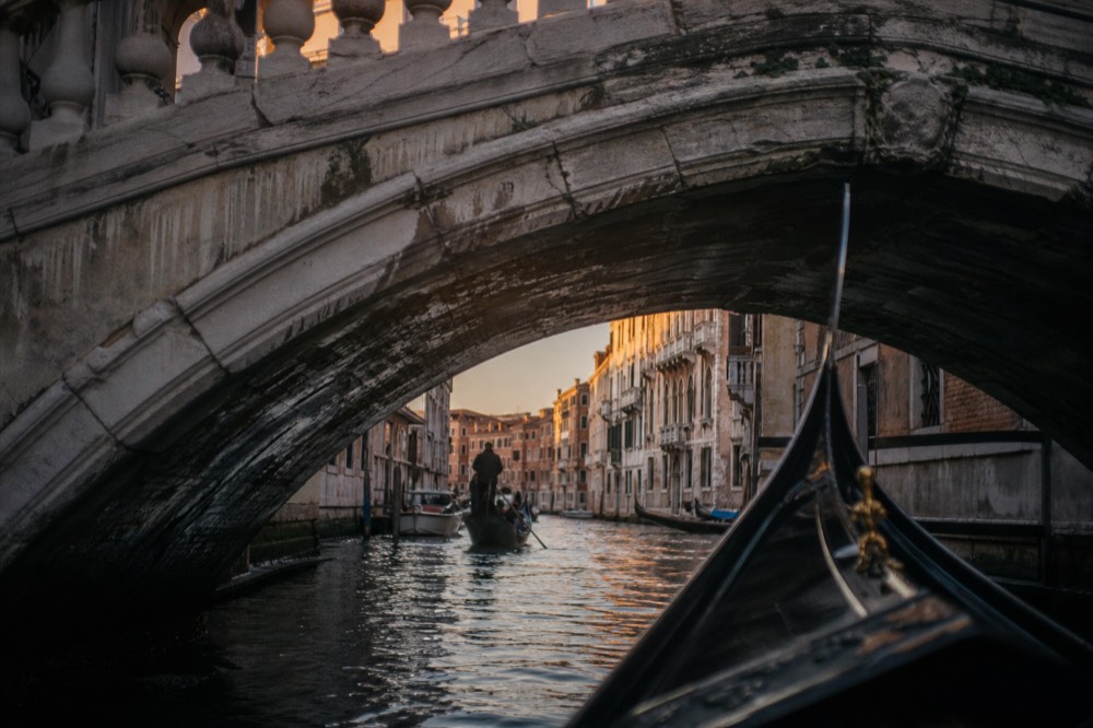 Stone bridge arch photographed from a boat passing beneath, wet stonework and the bright canal opening on the far side
