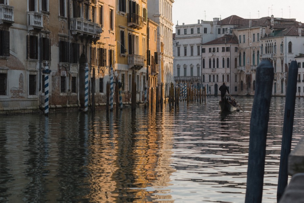 Empty canal water at first light with mooring poles casting long reflections and shuttered palace windows above