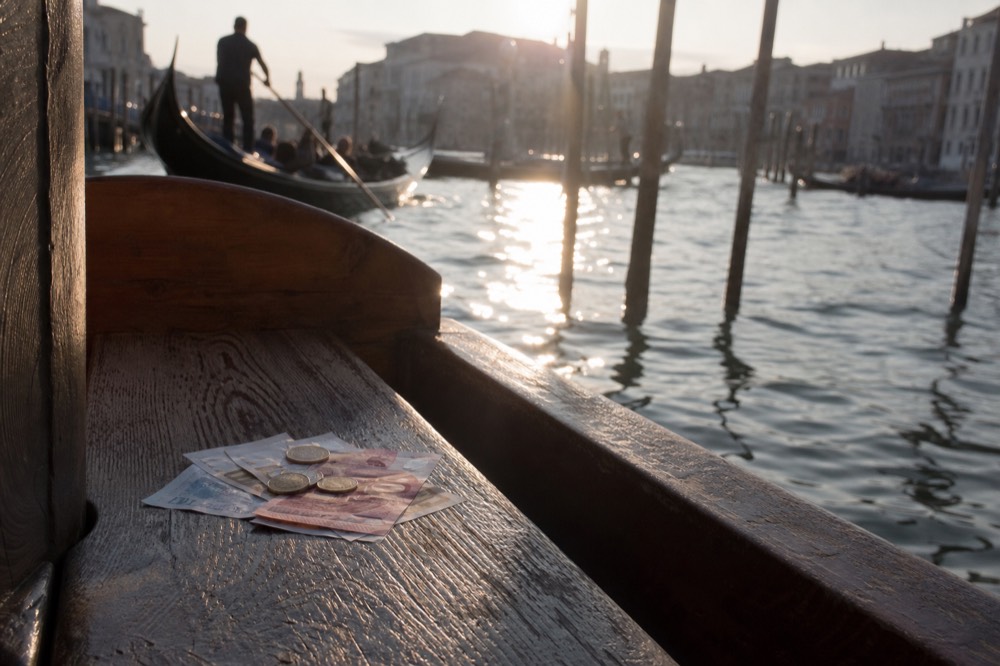 Euro banknotes and a few coins resting on a weathered wooden bench seat with dark canal water visible beyond the gunwale