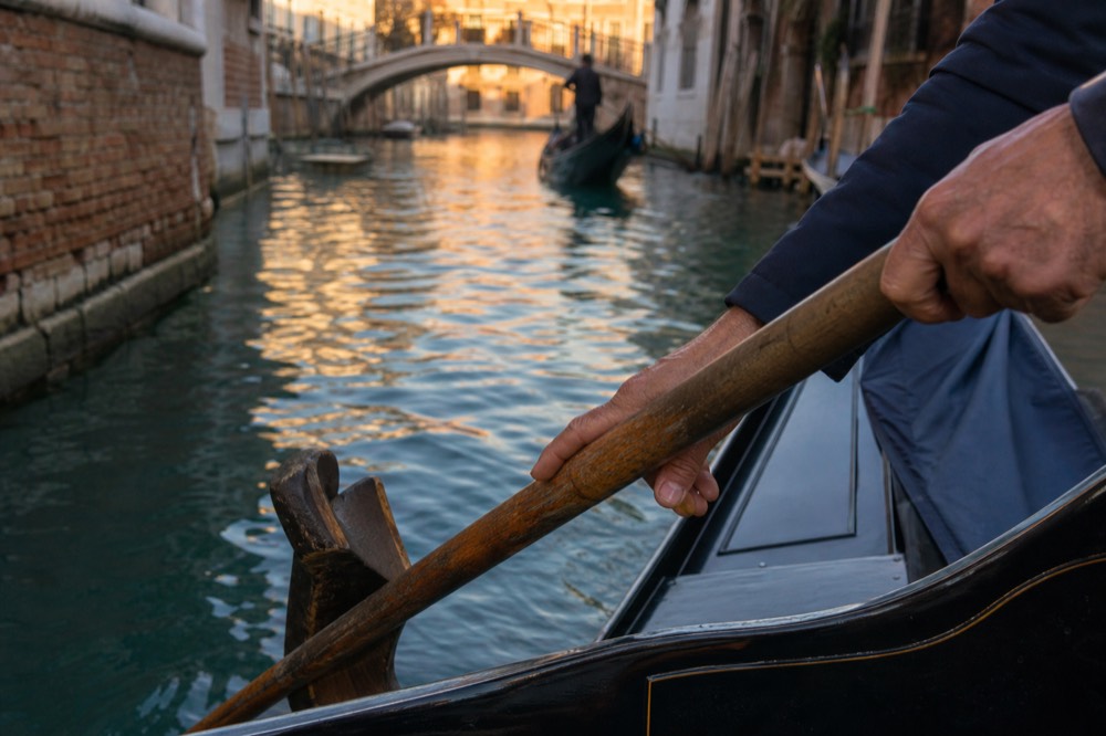 Close view of a gondolier's hands on a worn wooden oar resting in its carved forcola, canal water sliding past below